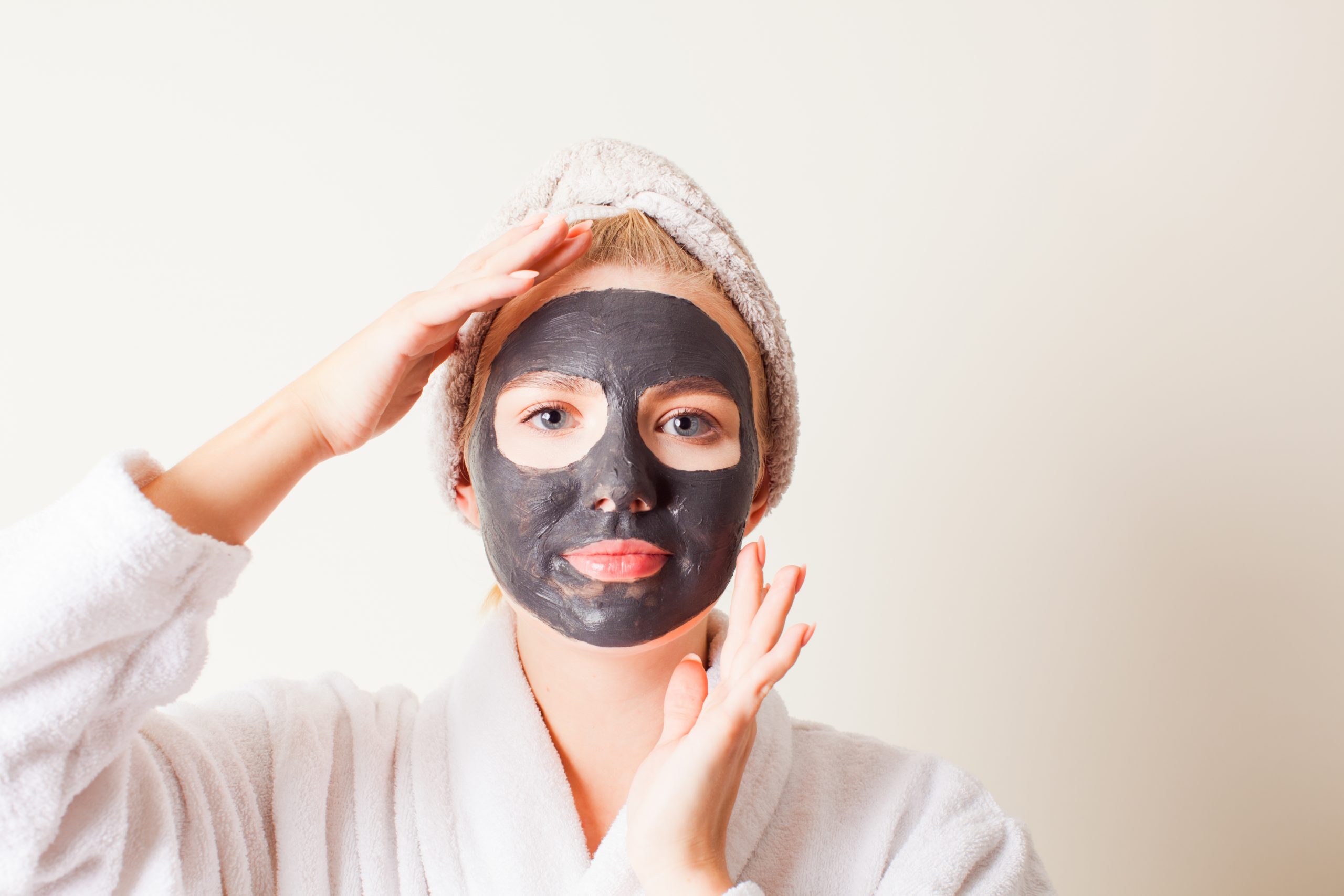 Woman using a black face mask, close up face with hands. Spa treatment