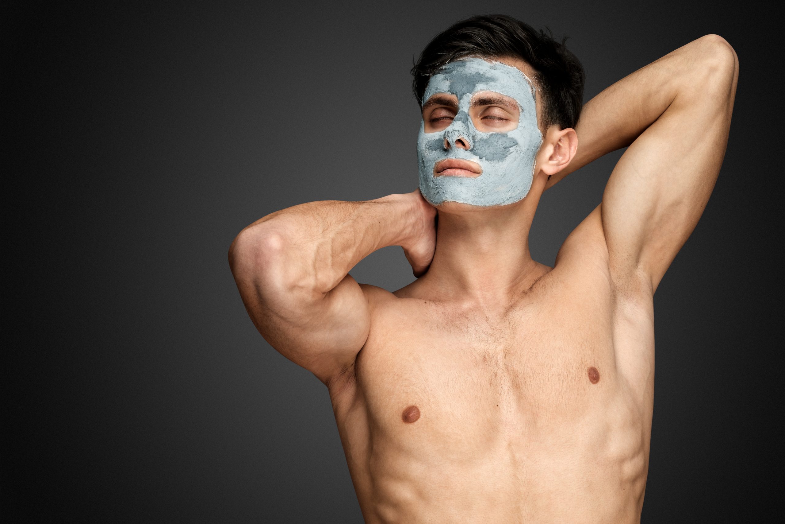 Portrait of a beautiful relaxed young man with a facial mud clay mask, face and body skin care treatment.