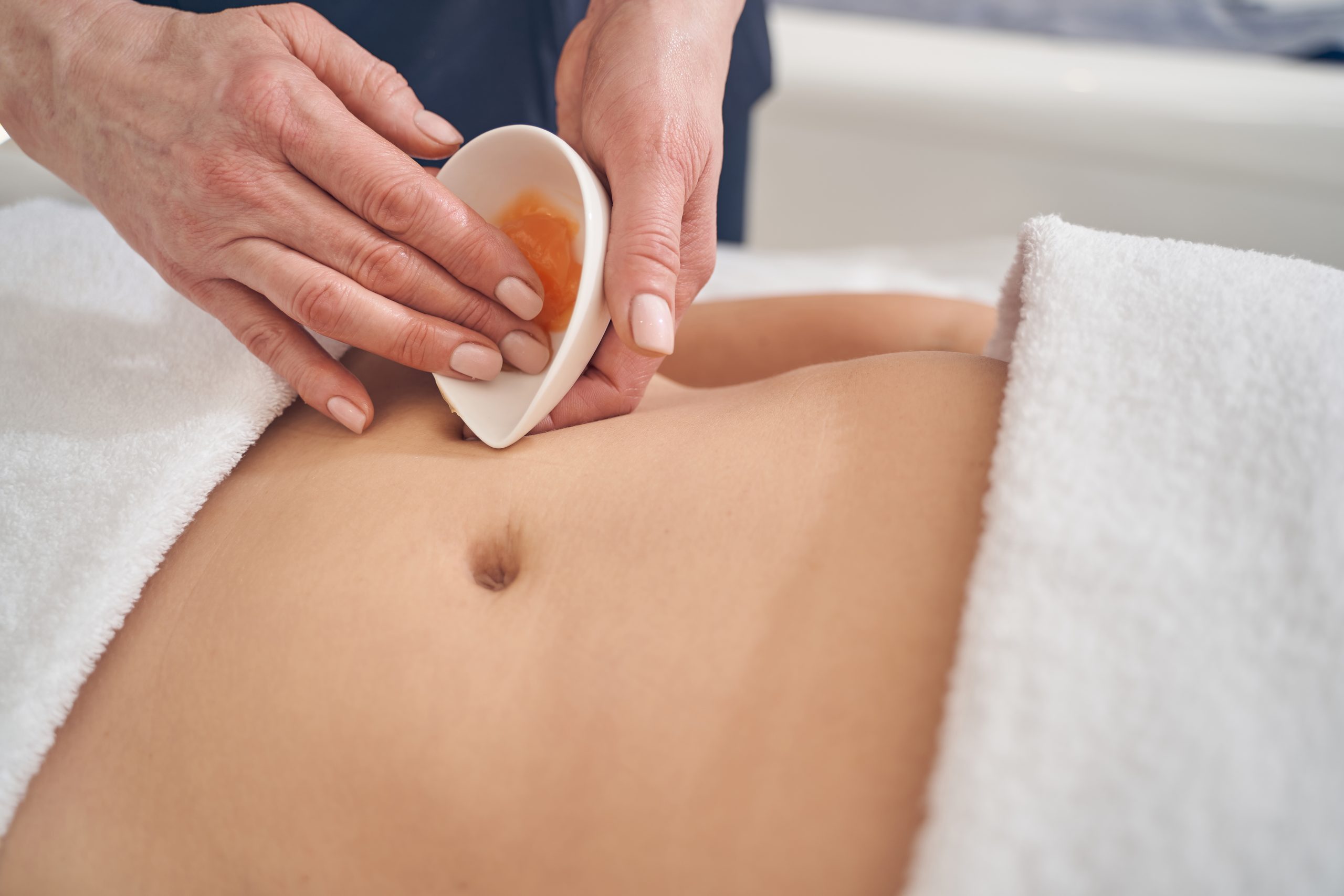 Close up of a woman belly and hands of massage therapist taking nourishing cream from the bowl