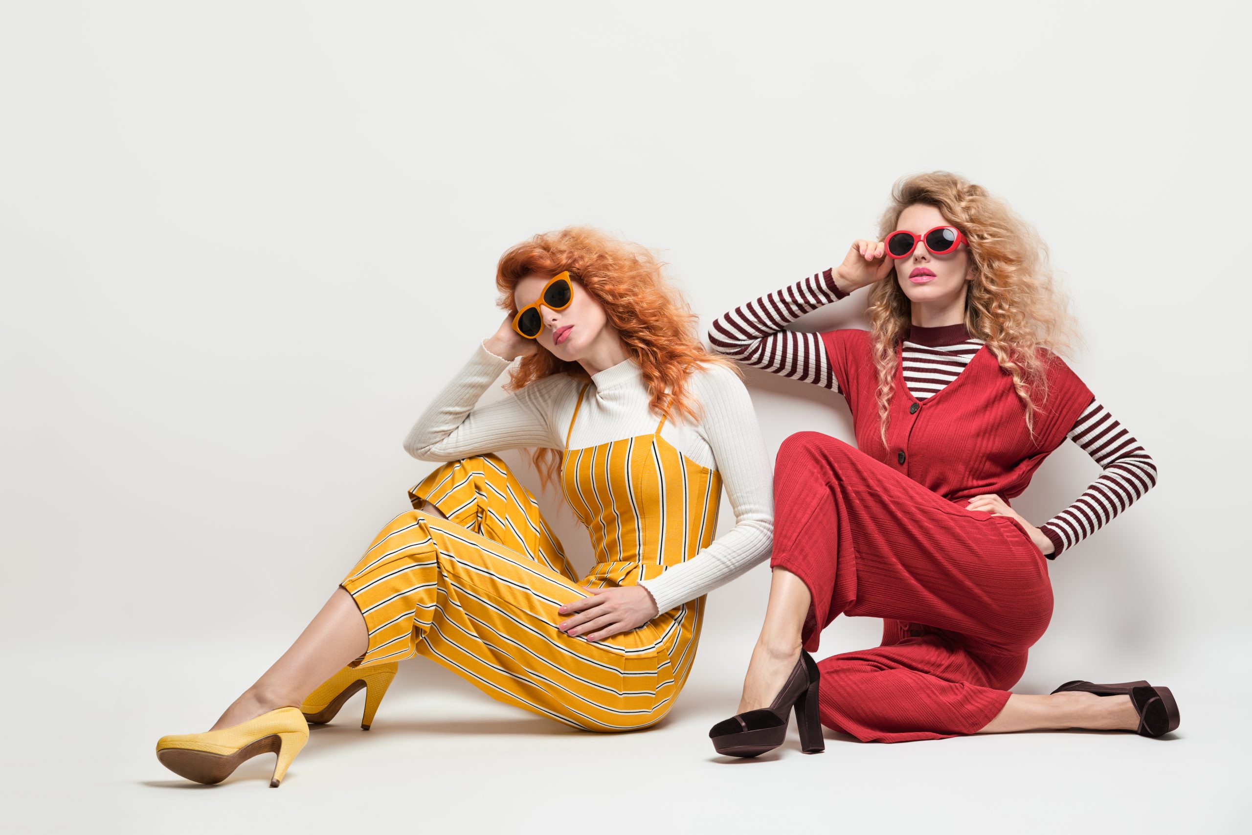 Fashion. Gorgeous Woman in Red Yellow jumpsuit, Sunglasses, heels. Creative Elegant Style. Two Sexy Girl in Trendy Outfit with Curly Hairstyle. Young Playful Sisters Friends. Creative Vintage