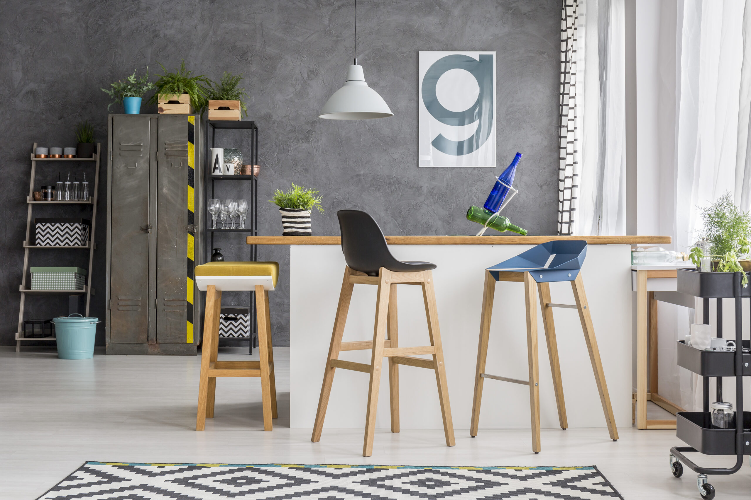 Wooden bar stools at kitchen island in bright kitchen with lamp and poster on concrete wall