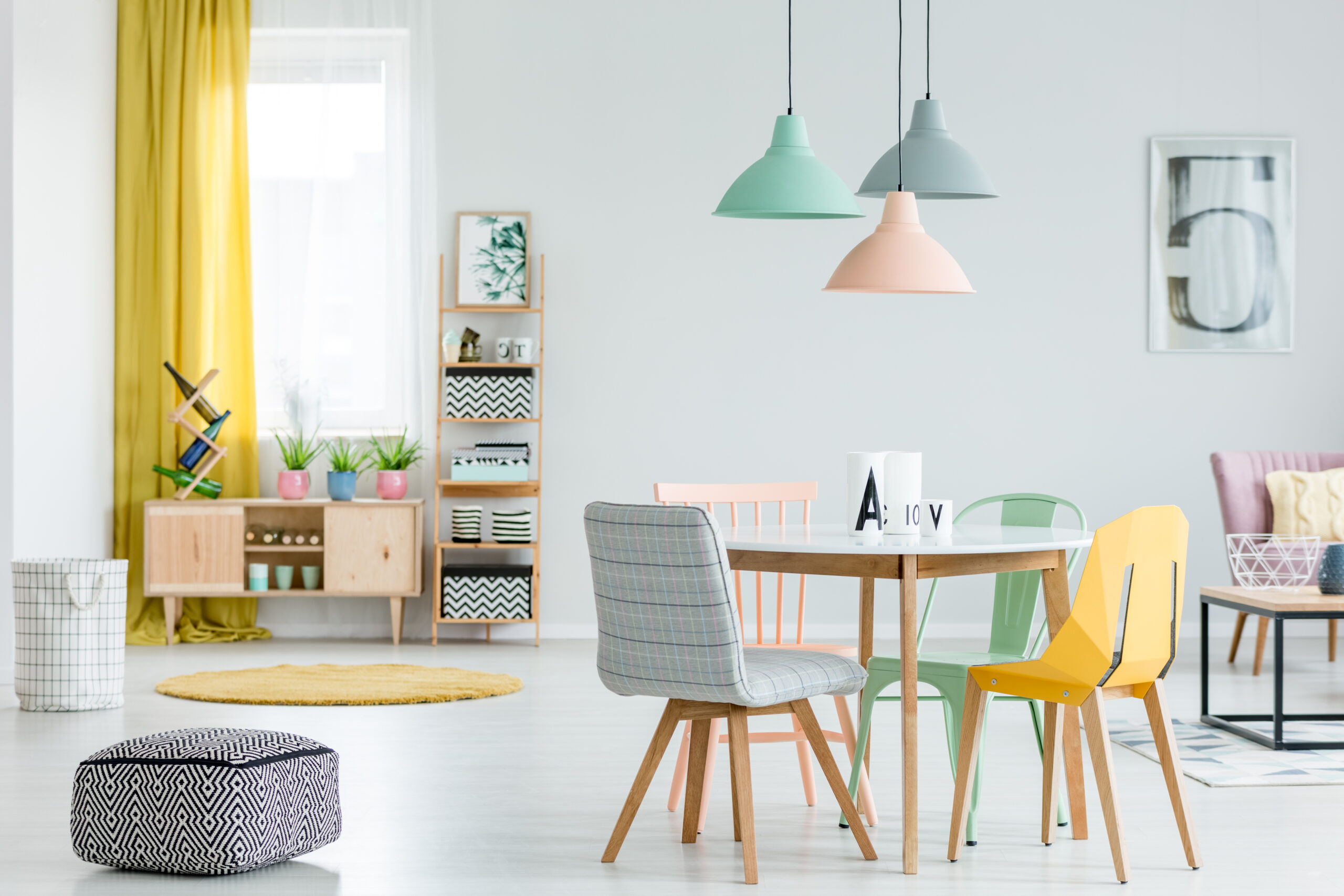 Feminine dining room interior with colorful chairs at the round table and wooden cupboard near the window with yellow drapes