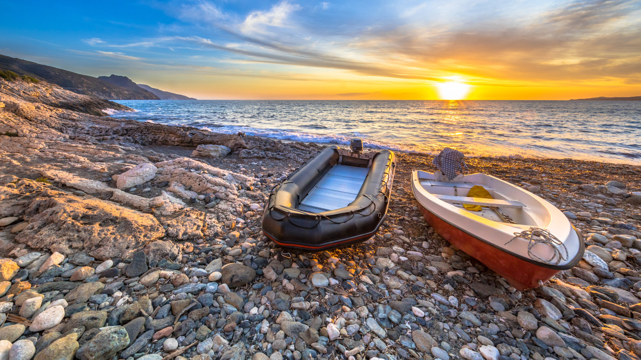 Two boats at sunset on a pebble beach on Cap Corse, Corsica, France.