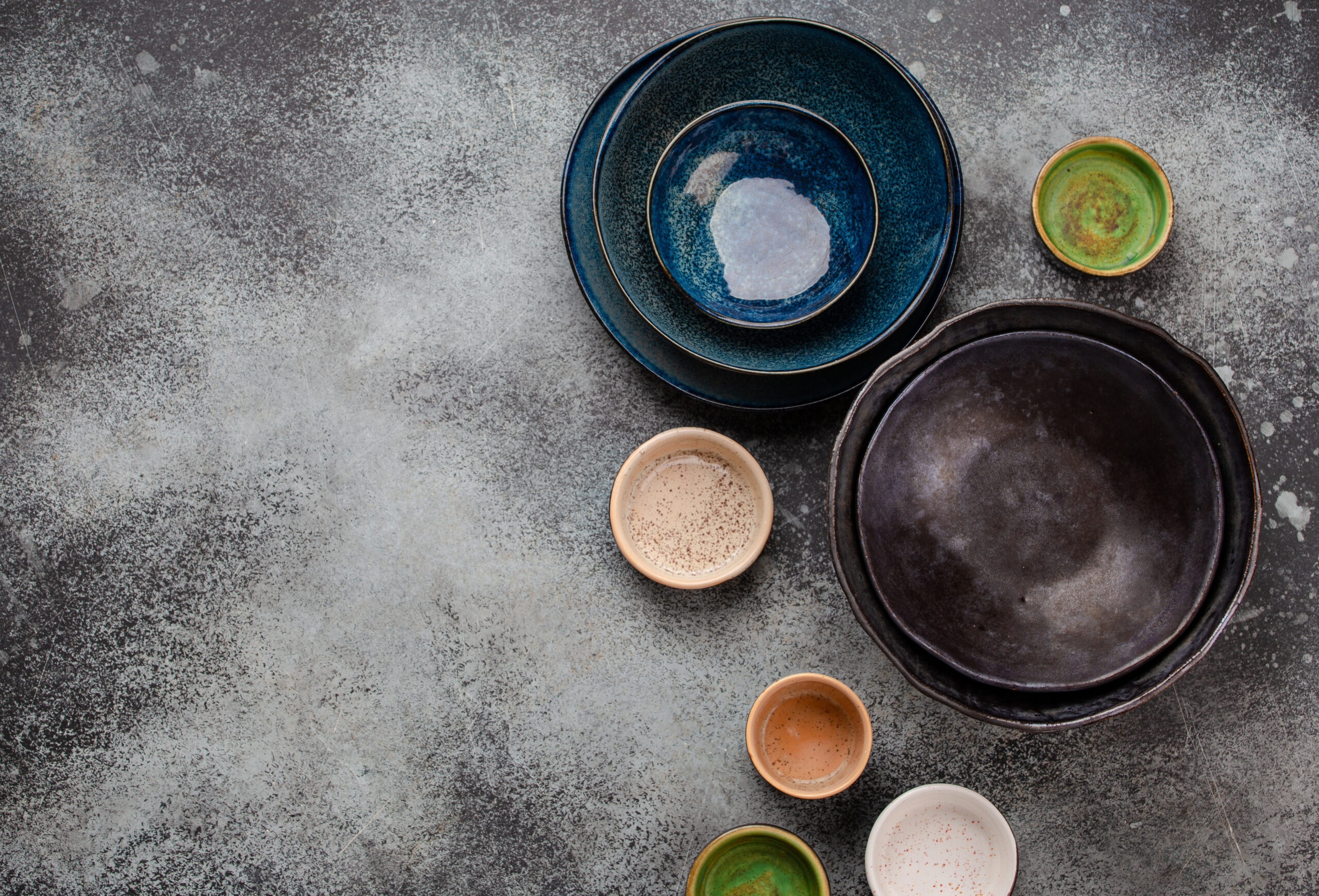 Assorted ceramic hand-made multicolored empty plates and bowls on rustic gray concrete background. Rustic table setting, set of plates. Top view of beautiful empty plates and bowls with space for text