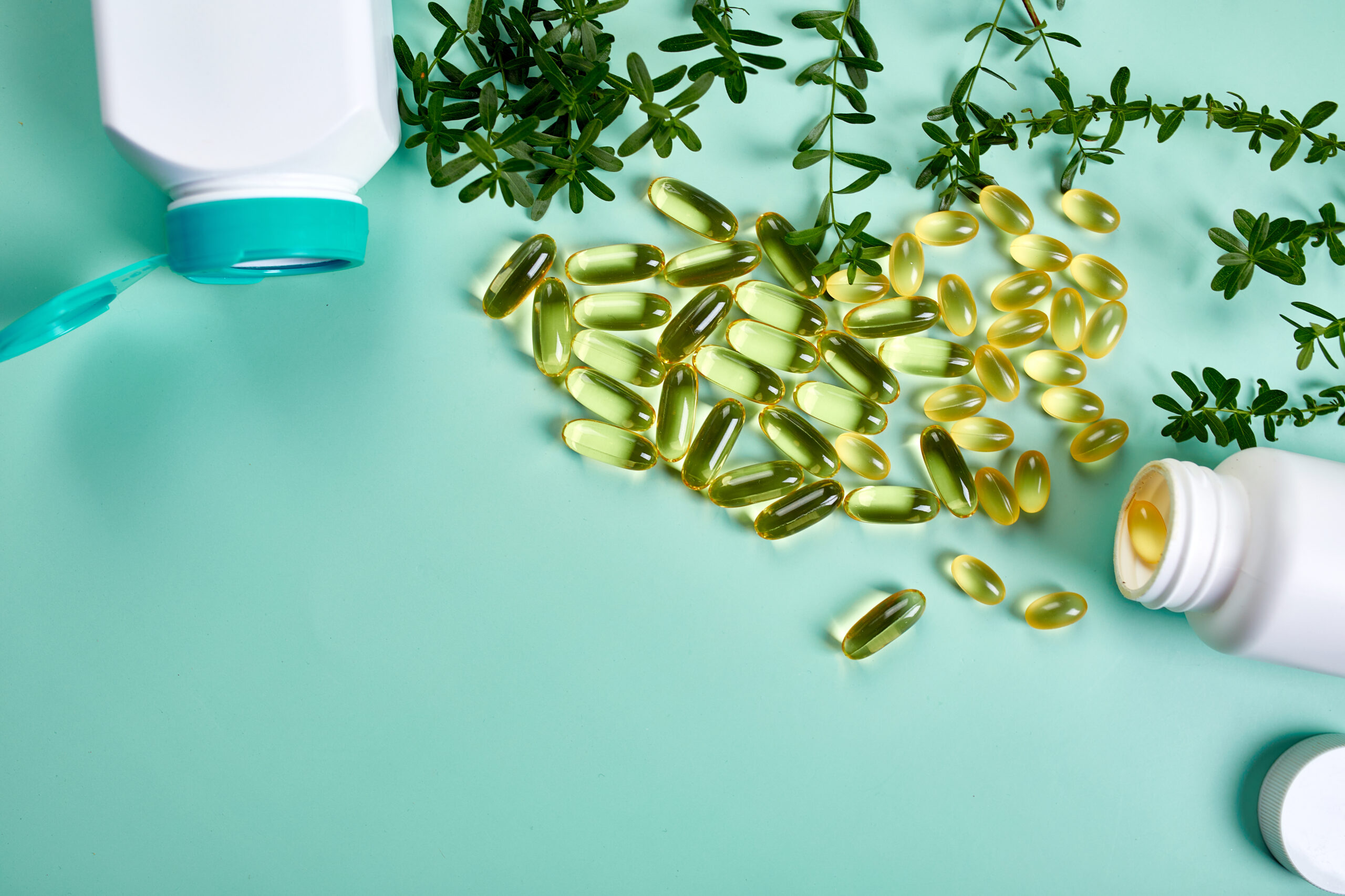 Capsules with fish oil and green leaves on green background, Healthcare concept, healthy food, Top view, copy space.